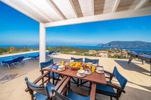 A terrace with a pool, dining table, chairs, and a view of the sea. - Villa Ireni Fiskardo by Villa Plus (Ionian Islands)