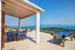 Une table de billard avec une vue dégagée sur la mer et les montagnes, un espace de détente couvert avec des chaises et une piscine.
