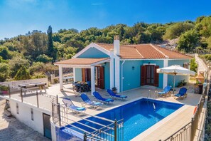A two-story house with a swimming pool, outdoor seating, and a view of the surrounding forest.