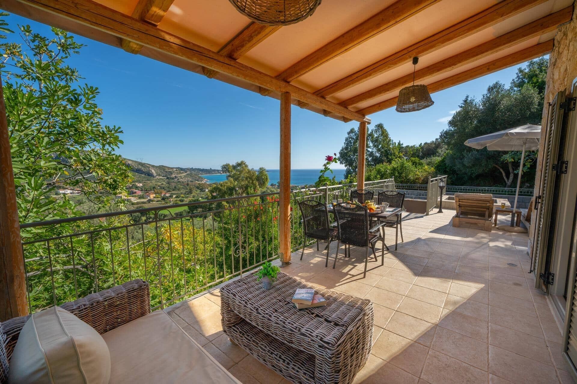 A covered outdoor patio with wicker furniture, a table with a book, and a view of the sea and hills.
