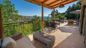 A covered outdoor patio with wicker furniture, a table with a book, and a view of the sea and hills.