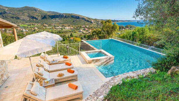 A pool with a view of the sea and mountains, lounge chairs, and a pergola.