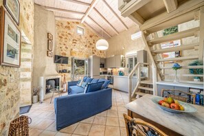 A rustic interior with a stone wall, a blue sofa, a kitchen area, and a staircase.