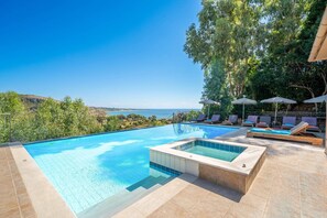 A swimming pool with a view of the sea, surrounded by lounge chairs and umbrellas.