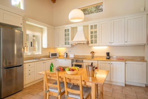 Una cocina con armarios blancos, un refrigerador de acero inoxidable, un microondas, una estufa y una mesa de comedor con dos sillas.