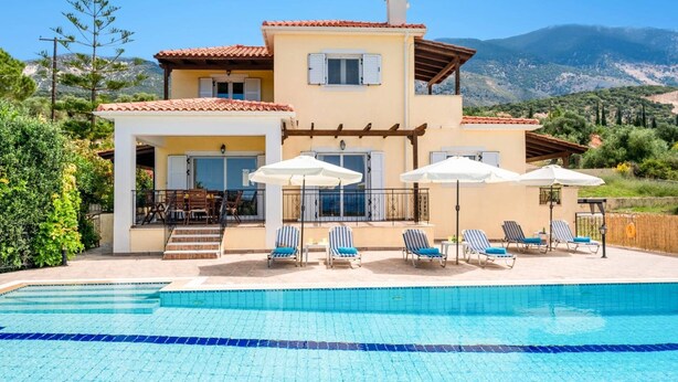 Una casa de dos plantas con piscina, mobiliario exterior y vistas a las montañas.