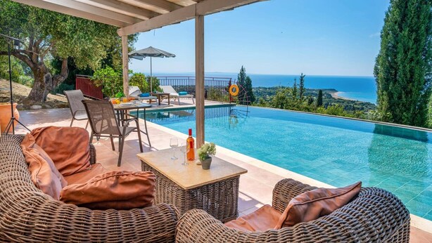 Ein Poolbereich mit Korbmöbeln, einem Tisch mit Flasche und Gläsern und Blick aufs Meer.