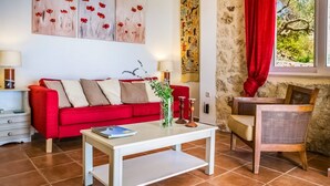 Ein Wohnzimmer mit einem roten Sofa, einem weißen Couchtisch und einem Holzstuhl. An den Wänden befinden sich Kunstwerke und eine Wandteppich.