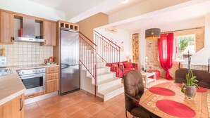Eine moderne Küche mit einem Edelstahl-Kühlschrank, einem Herd und Holzschränken. Eine rote Treppe führt zu einem Essbereich mit einem roten Tisch und Stühlen.