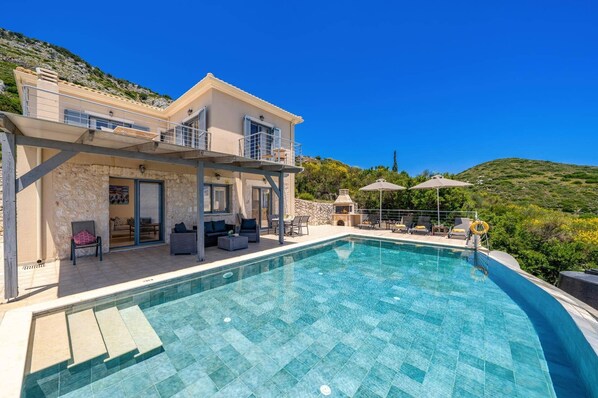 Une maison à deux étages avec une piscine, un espace salon extérieur et un mur en pierre.