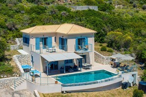 Une maison à deux étages dotée d’une piscine, d’un espace salon extérieur et d’un mur de pierre qui entoure la propriété.