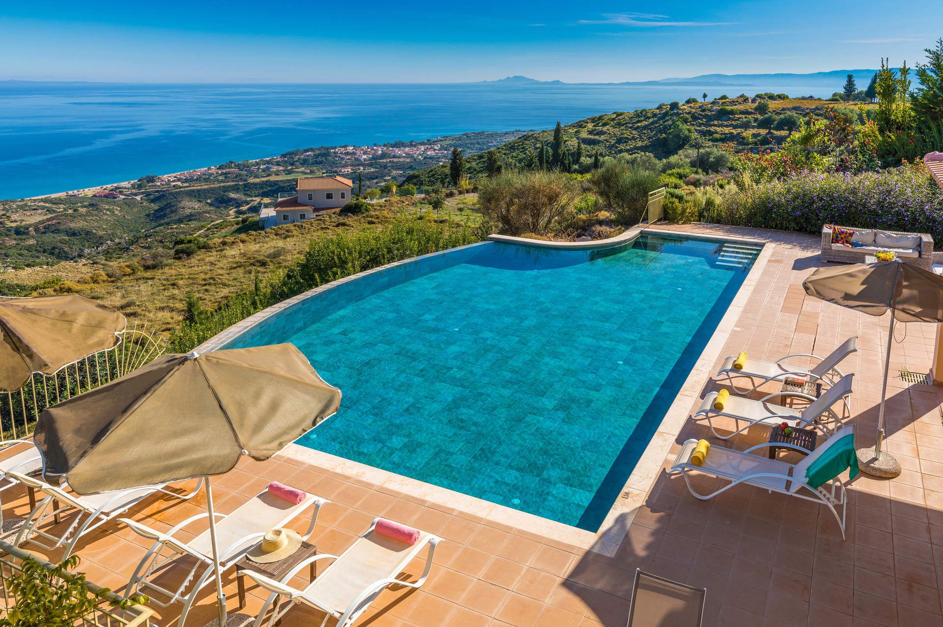 A clear blue swimming pool with a view of the sea and hills.