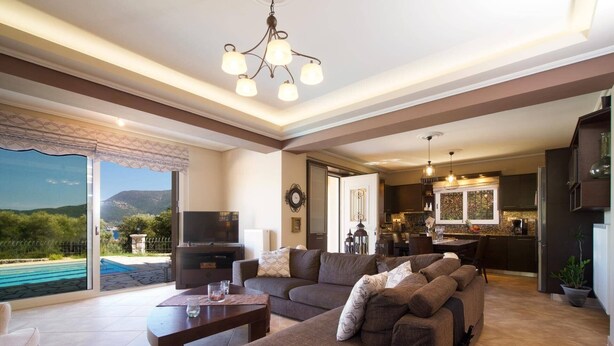 Amplia sala de estar con un sofá grande, un televisor y un comedor con cocina al fondo.