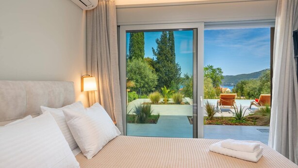 Quarto de hotel com cama, mesa de cabeceira, luminária e vista para a piscina e jardim.