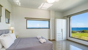 Un dormitorio con cama, ventana con vista al mar, armario y lámpara.