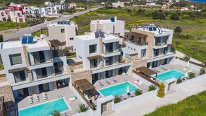 Una villa moderna con dos piscinas, fachadas de piedra y vistas al paisaje circundante.