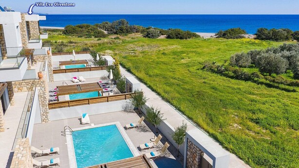 Una villa con varias piscinas y tumbonas, rodeada de exuberante vegetación y vistas al mar.