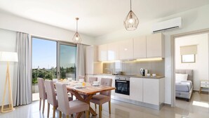 Una cocina moderna con armarios blancos, horno empotrado y comedor con mesa y sillas de madera.