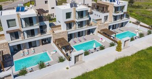 Una villa moderna con dos piscinas, fachadas de piedra y vistas al paisaje circundante.