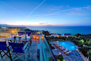 Una terraza en la azotea con zona de comedor, sillones de descanso y piscina con vistas al mar.