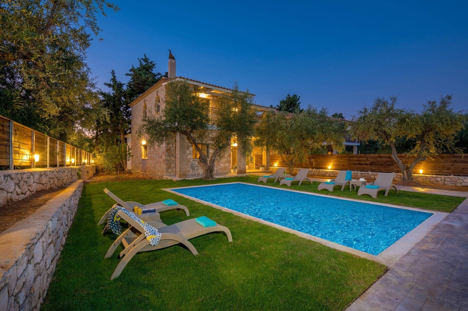 Ein Schwimmbecken mit Liegestühlen und ein Steinhaus mit warmer Beleuchtung.