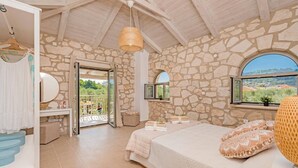 Ein Schlafzimmer mit Stehwänden, einem Bett mit gesteppter Bettdecke, einer hängenden Rattanlampe und Blick auf die Landschaft durch ein Fenster.