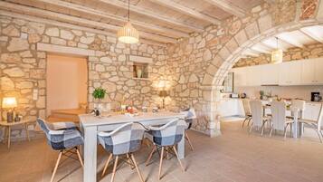 Une salle à manger aux murs de pierre et au plafond en bois, une table dressée pour quatre personnes et une cuisine en arrière-plan.