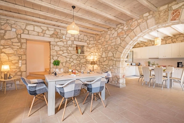 A stone-walled dining area with a wooden ceiling, a table set for four, and a kitchen in the background.