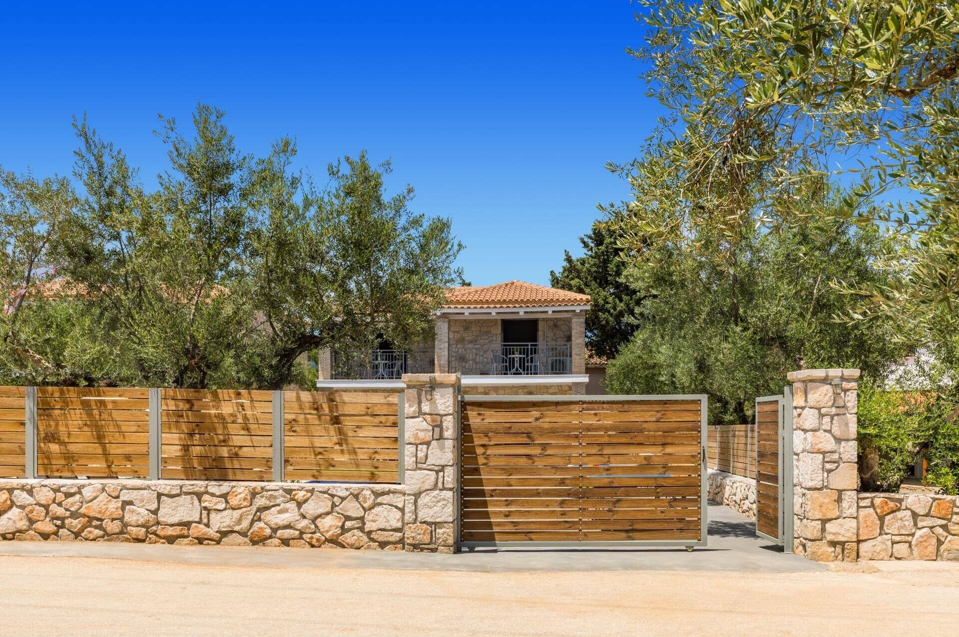 A stone-walled house with a tiled roof, a wooden gate, and a stone wall.