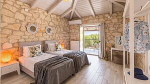 Een slaapkamer met twee bedden, stenen muren, een balkon en een plafondventilator.