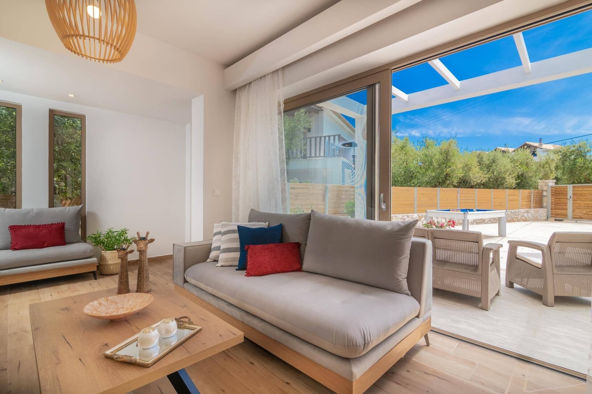 A modern living room with a sofa, a coffee table, and a dining area with outdoor furniture.