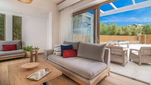 A modern living room with a sofa, a coffee table, and a dining area with outdoor furniture.