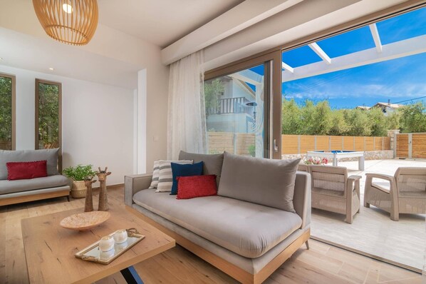 A modern living room with a sofa, a coffee table, and a dining area with outdoor furniture.