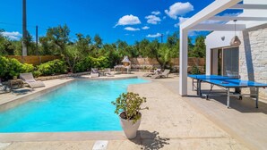 A swimming pool with lounge chairs, a barbecue area, and a ping pong table in a sunny outdoor setting.