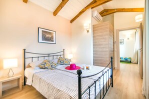 Ein Schlafzimmer mit einem Bett, Nachttischlampen, einem gerahmten Bild an der Wand und einer Holztür zu einem anderen Raum.