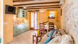 A cozy living area with a sofa, a dining table, and a kitchen area with cabinets and a TV. - Villa Fumica by Villa Plus (Radetići)