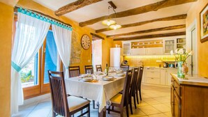 A dining area with a table set for four, wooden chairs, a clock on the wall, and a kitchen in the background. - Villa Fumica by Villa Plus (Radetići)