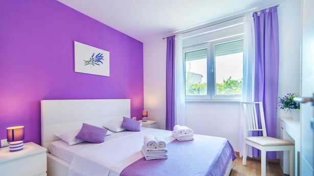 A bedroom with a bed, nightstands, a chair, and a window with curtains. - Villa Ladonja by Villa Plus (Pula)