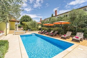A swimming pool with lounge chairs and umbrellas, surrounded by greenery and a building with a tiled roof. - Villa Ladonja by Villa Plus (Pula)