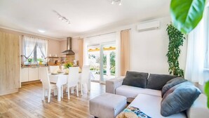 A modern living room with a grey sofa, a dining area with white chairs, and a kitchen with a large window. - Villa Ladonja by Villa Plus (Pula)
