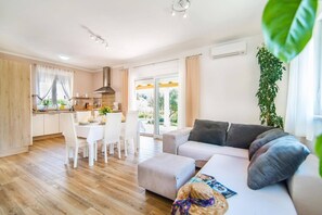 A modern living room with a grey sofa, a dining area with white chairs, and a kitchen with a large window. - Villa Ladonja by Villa Plus (Pula)