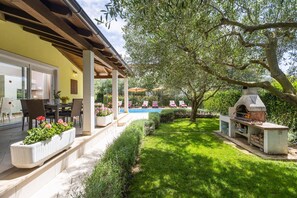 Eine Terrasse mit Sitzgelegenheiten im Freien, einem Pool und einer Grillanlage.