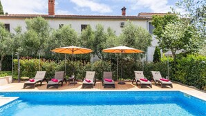 A swimming pool with lounge chairs and umbrellas, surrounded by greenery and a building with a tiled roof. - Villa Ladonja by Villa Plus (Pula)
