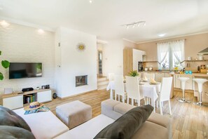 Ein modernes Wohnzimmer mit Flachbildfernseher, Kamin und Essbereich mit weißen Stühlen und Tisch.