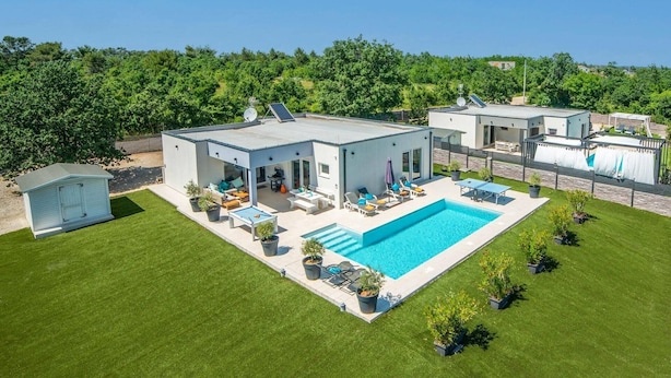 Una casa moderna con piscina, mobiliario de exterior y jardín.