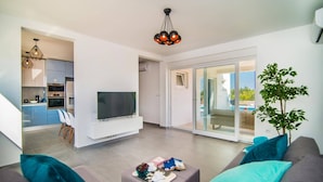 Una sala moderna con televisor de pantalla plana, un sofá y una zona de comedor con cocina al fondo.