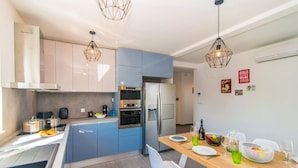Una cocina moderna con armarios azules, un refrigerador de acero inoxidable y un comedor con una mesa de madera lista para dos personas.