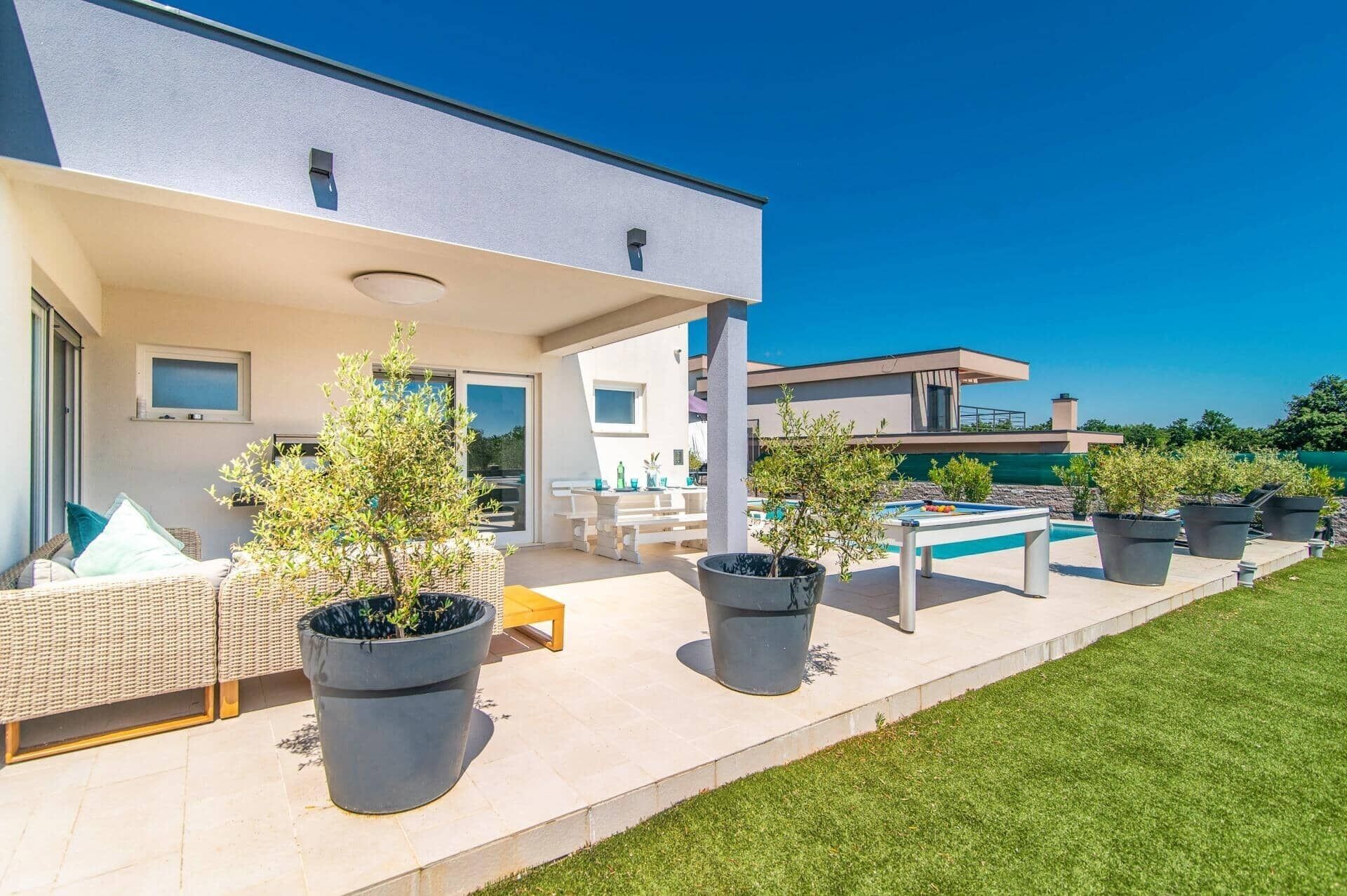 Une maison moderne dotée d’un patio couvert, d’un espace salon extérieur et d’une piscine.