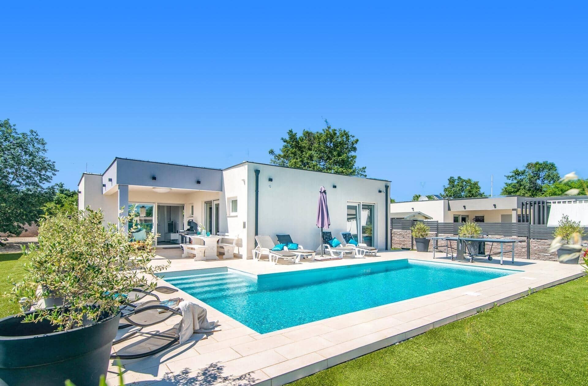 A modern house with a swimming pool, outdoor seating, and a patio area.