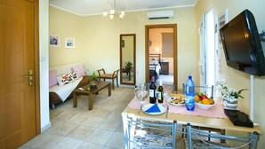 A cozy living room with a sofa, a dining table set with a bottle of wine, glasses, and a bowl of fruit. - Villa Jasmine Sostis by Villa Plus (Agios Sostis)